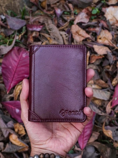 Premium Fenzo burgundy leather trifold wallet for men held against a natural autumn leaves background